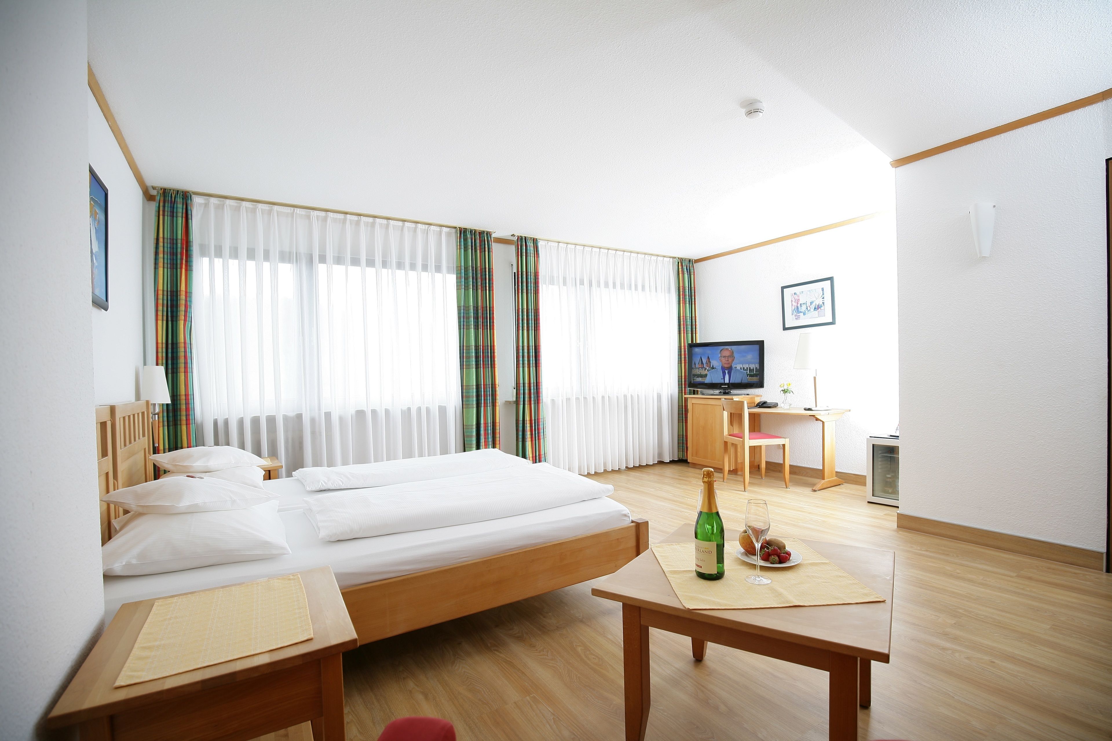 A hotel room with a bed, a desk, a television, and a window with curtains.