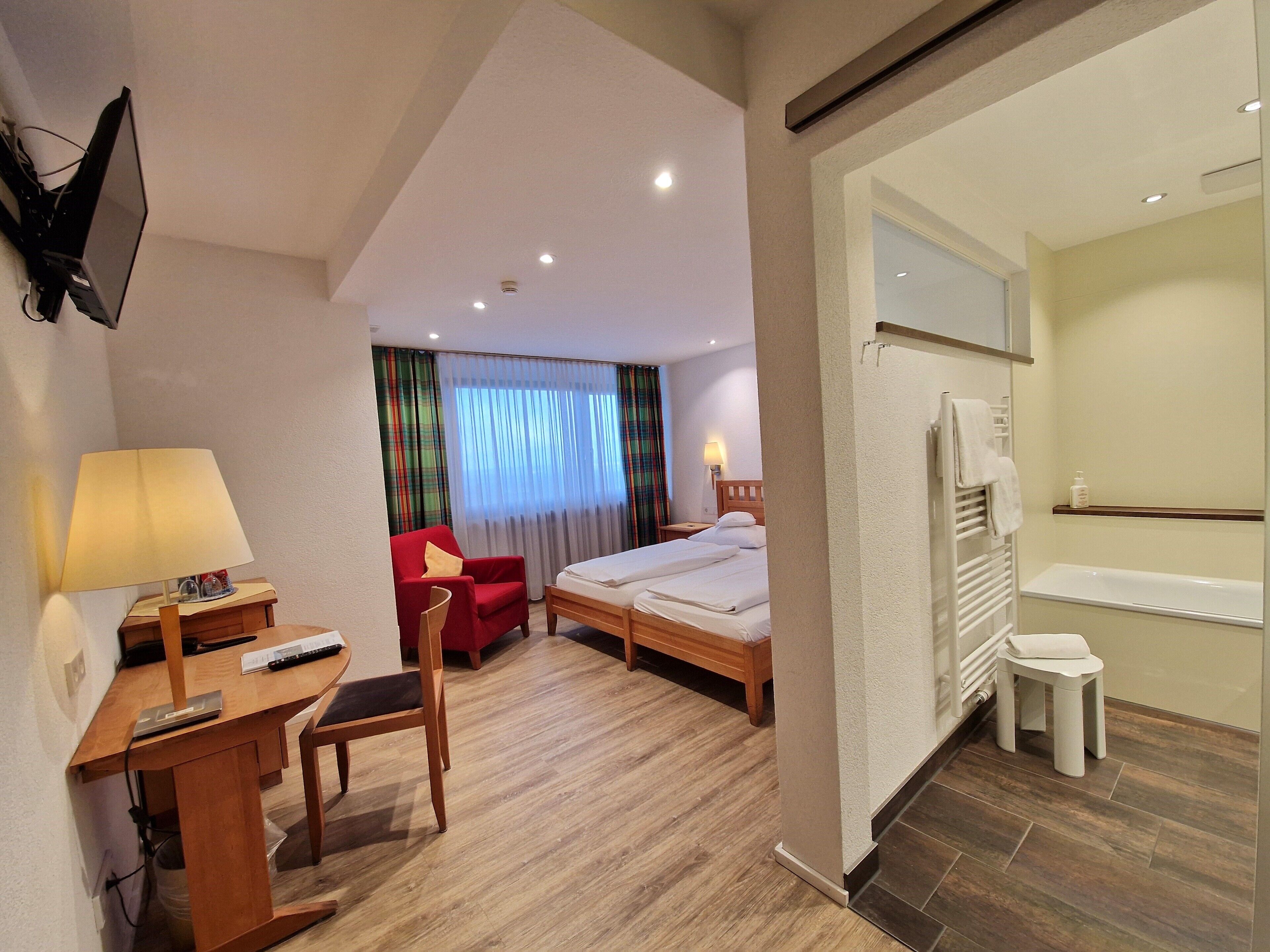 Habitación de hotel con escritorio, silla, cama y baño con bañera y retrete.