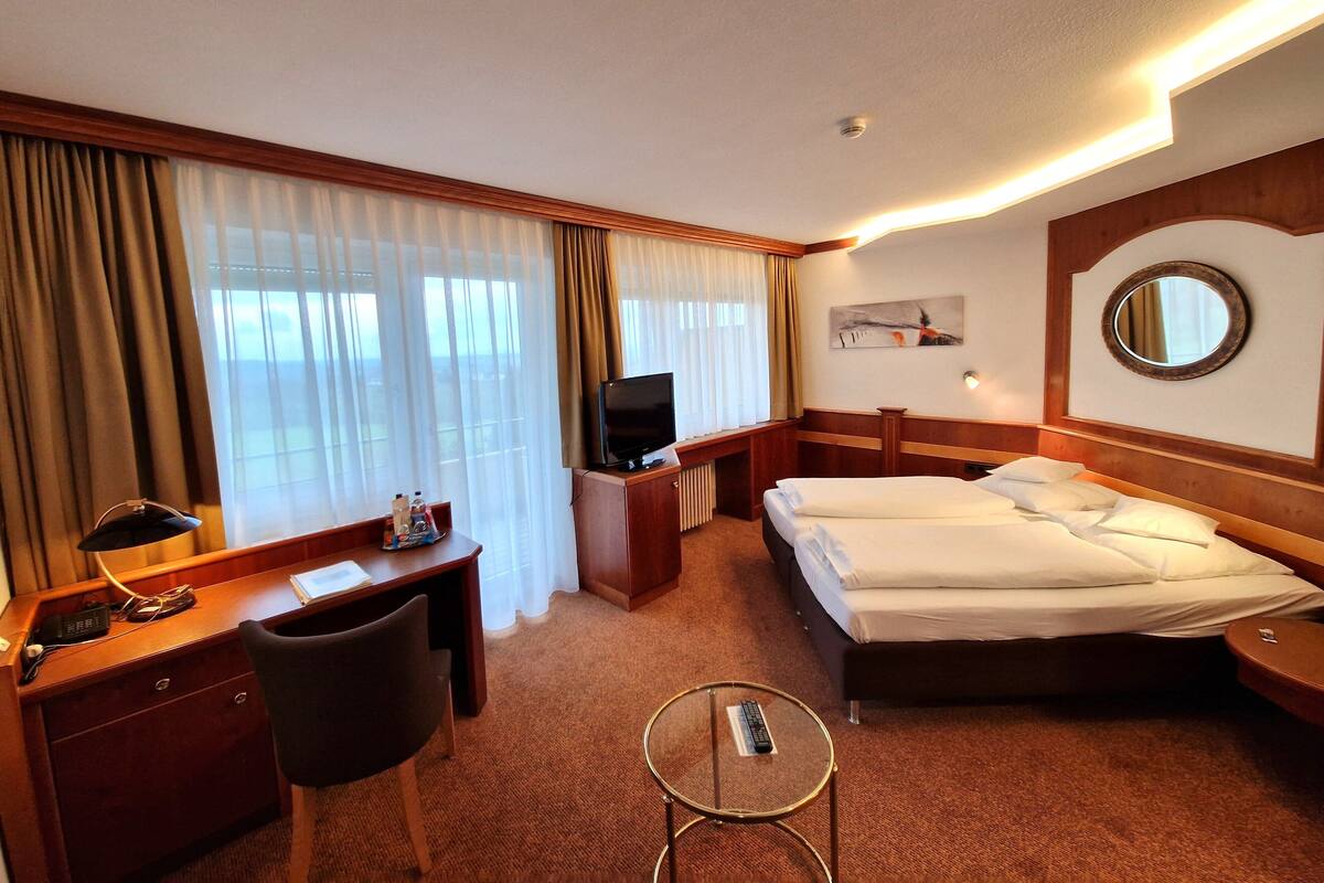 Habitación de hotel con cama, escritorio, silla, televisor y una mesita con control remoto.