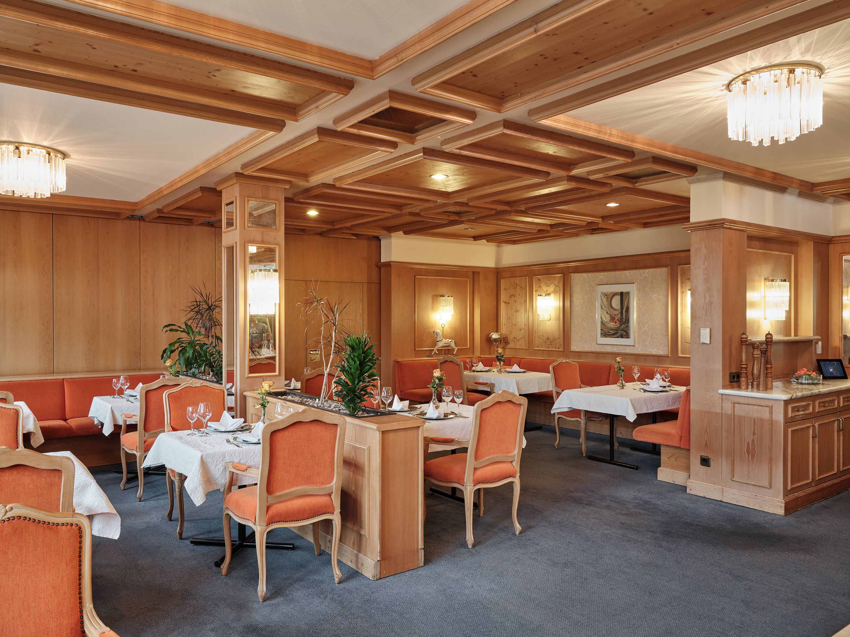 A restaurant with wooden paneling, tables with white tablecloths, and orange upholstered booths.