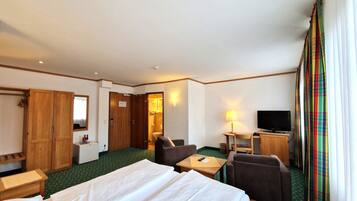 A hotel room with a bed, two chairs, a desk, a television, and a bathroom visible through an open door.