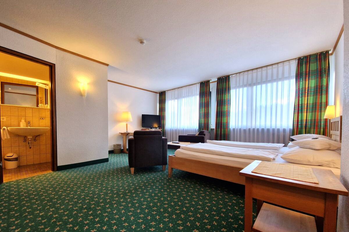 Habitación de hotel con cama, escritorio, silla, televisión, baño y ventana con cortinas.