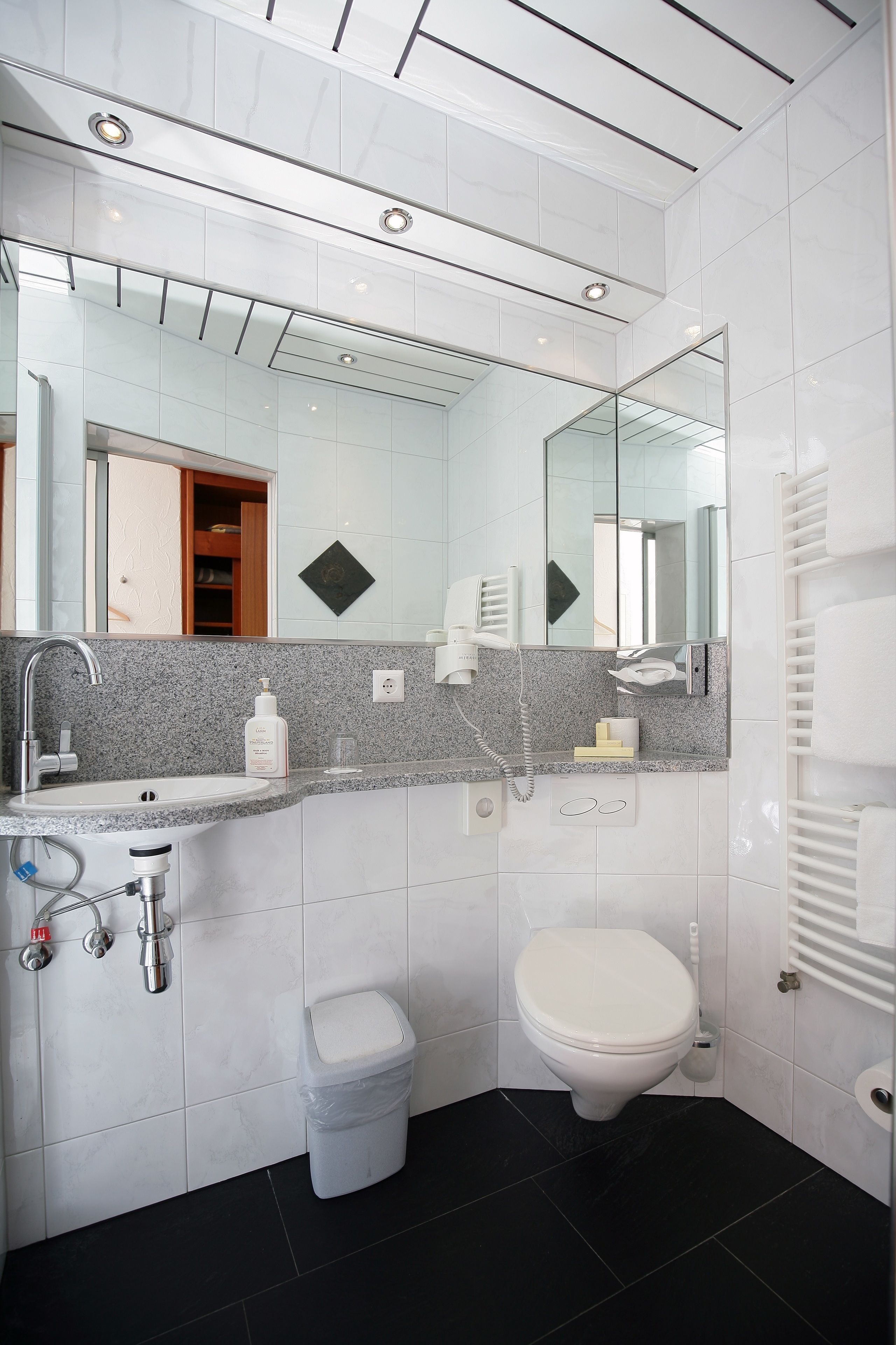Une salle de bain moderne avec un lavabo blanc, des toilettes, un miroir et un porte-serviettes.