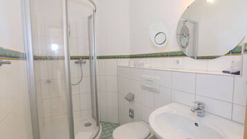Un baño con ducha de mampara de vidrio, inodoro y lavamanos.