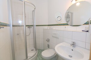 Un baño con ducha de mampara de vidrio, inodoro y lavamanos.