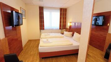 Een hotelkamer met een groot bed, twee nachtkastjes, een aan de muur bevestigde televisie en een raam met gordijnen.