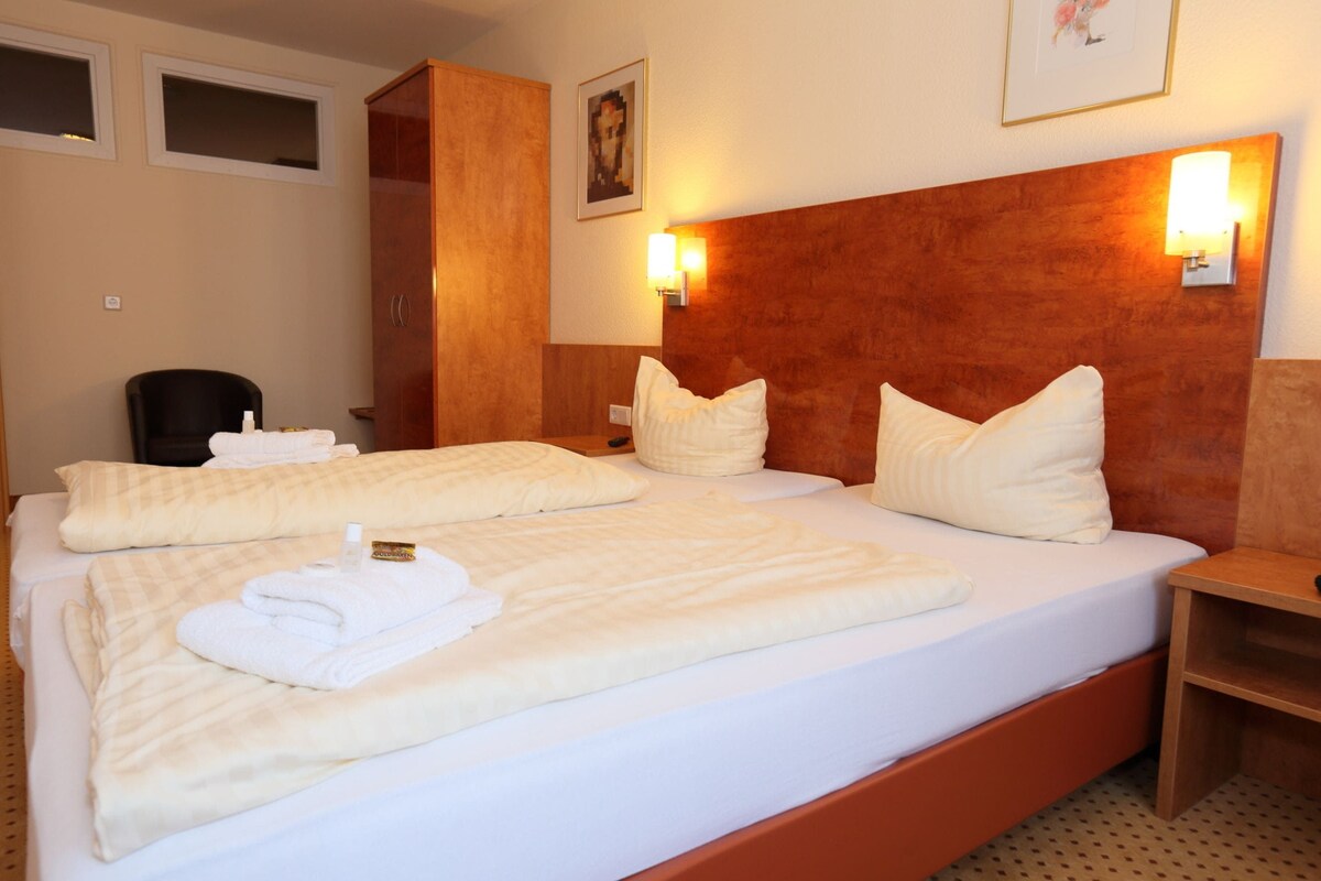 A hotel room with a large bed, two bedside tables, a wardrobe, and two wall-mounted lights.