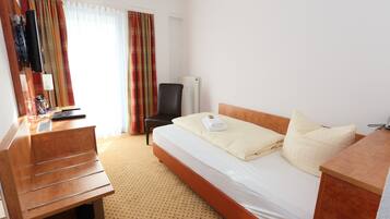 Een hotelkamer met een bed, een bureau, een stoel, een televisie en een raam met gordijnen.