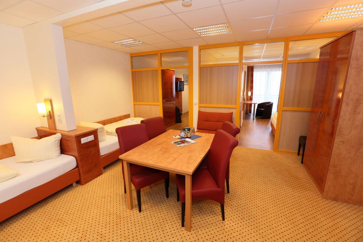 A hotel room with a wooden table, red chairs, a sofa, and a bed.
