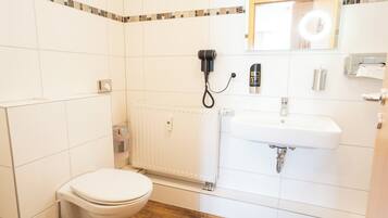 Ein Badezimmer mit Toilette, Waschbecken, Spiegel, Föhn und Handtrockner.