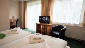 Habitación de hotel con dos camas, un escritorio, una silla, un televisor y ventanas grandes con cortinas.