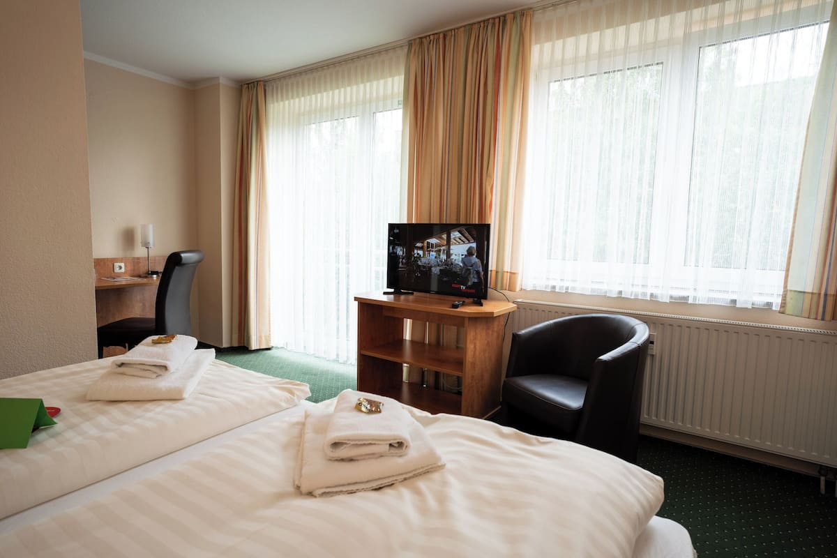 A hotel room with two beds, a desk, a chair, a television, and large windows with curtains.