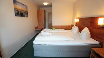 Habitación de hotel con cama, armario de madera, alfombra verde y un cuadro en la pared.