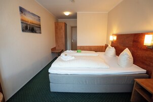 Habitación de hotel con cama, armario de madera, alfombra verde y un cuadro en la pared.