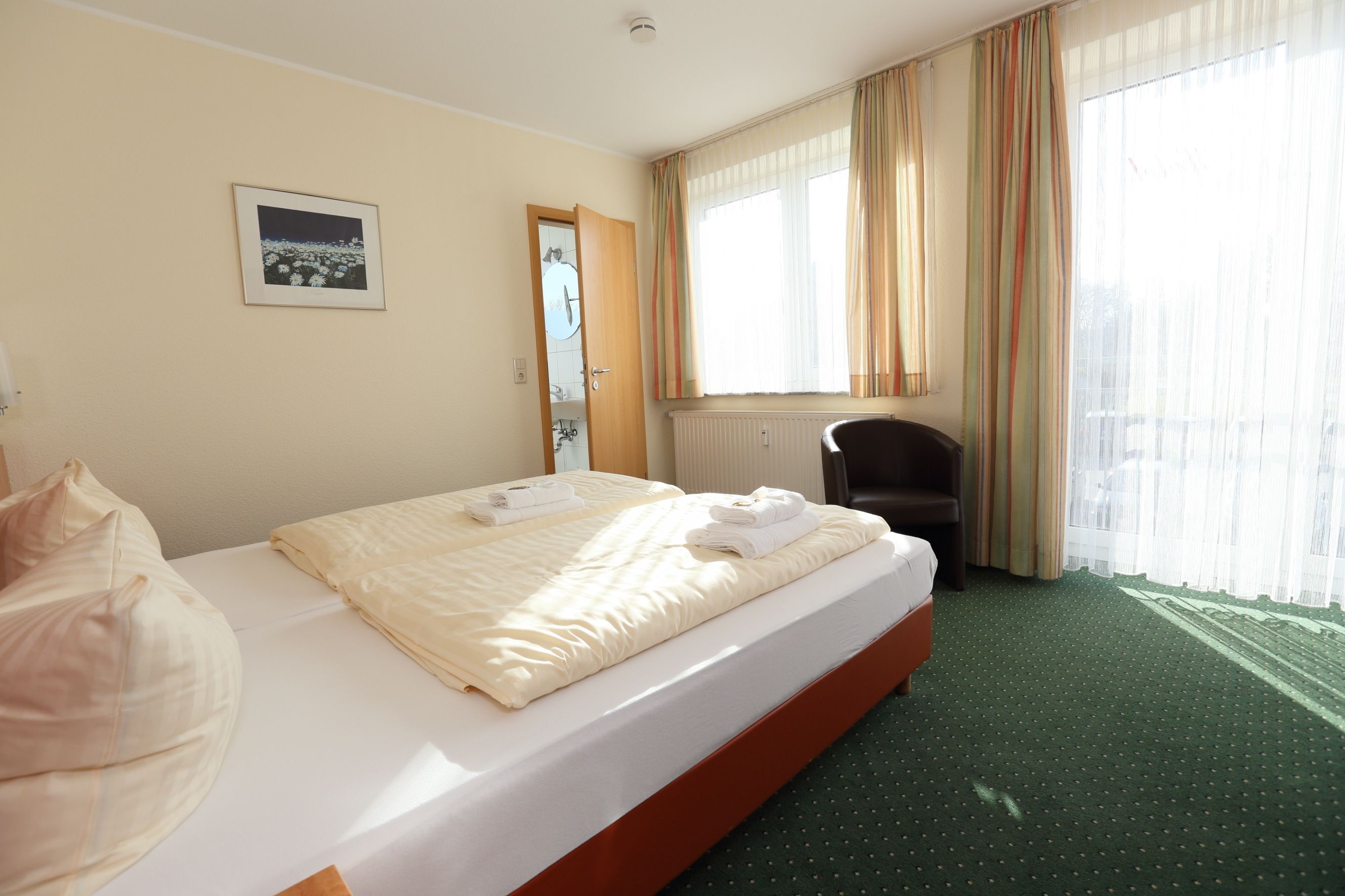 Una habitación de hotel con cama, una silla, ventana con cortinas e imagen en la pared.