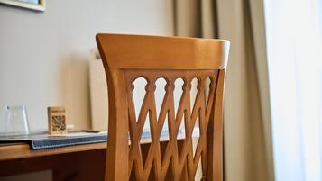 Uma cadeira de madeira com um design recortado peculiar, uma mesa com código QR e uma janela com cortinas ao fundo.