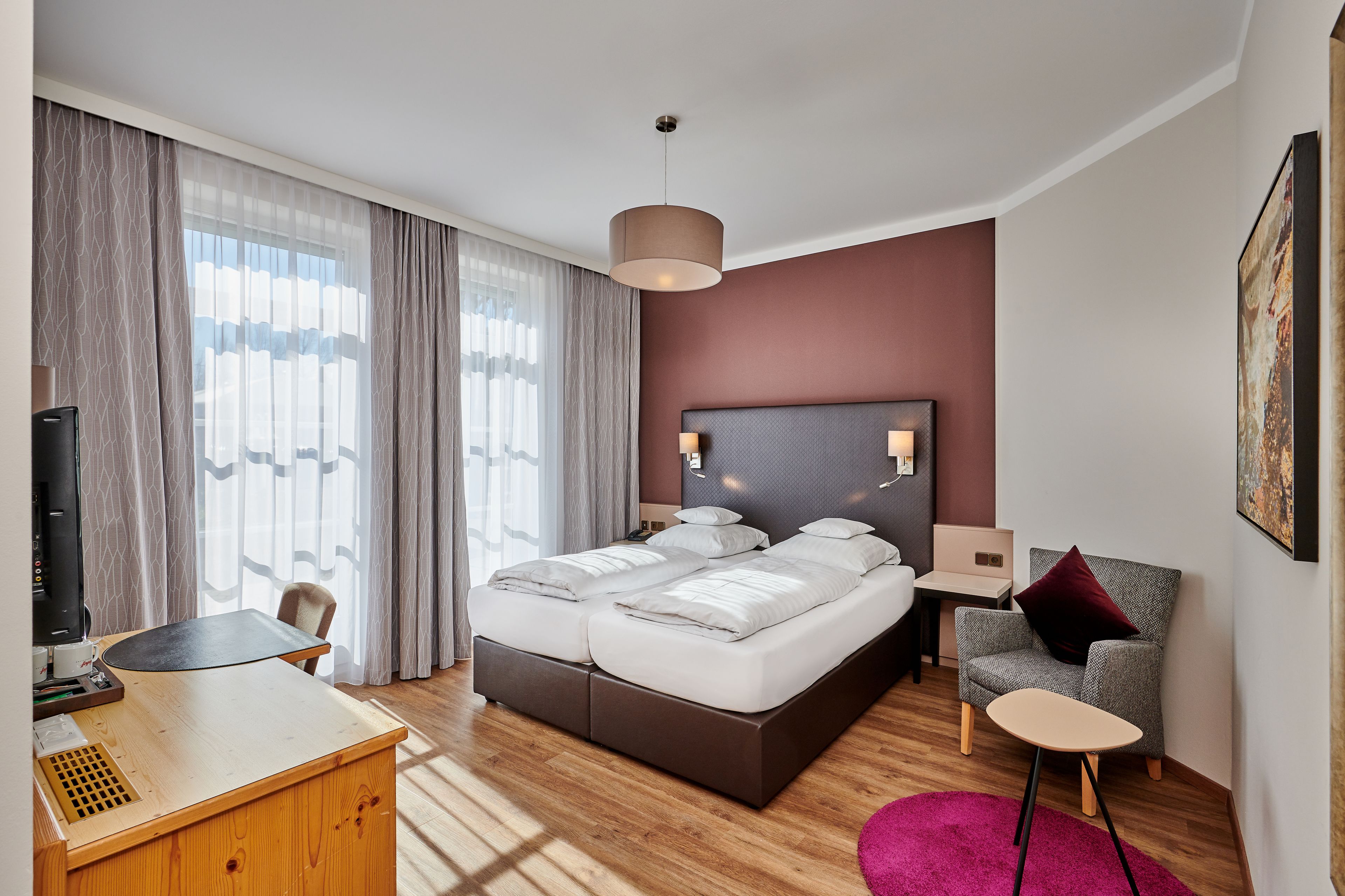A modern hotel room with a large bed, a desk, a chair, and a small table.