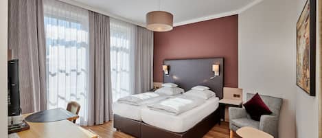 A modern hotel room with a large bed, a desk, a chair, and a small table.
