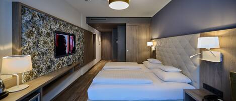 Una habitación de hotel moderna con una cama grande, un televisor de pantalla plana montado en una pared decorativa, una mesita de noche con lámpara y un cabecero de madera.