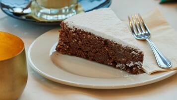 A slice of cake on a plate with a fork, a glass of coffee, and two golden bowls on a table.