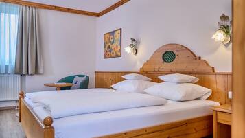 A wooden bed with white bedding, a small bedside table, a wall-mounted light fixture, and a painting of sunflowers.