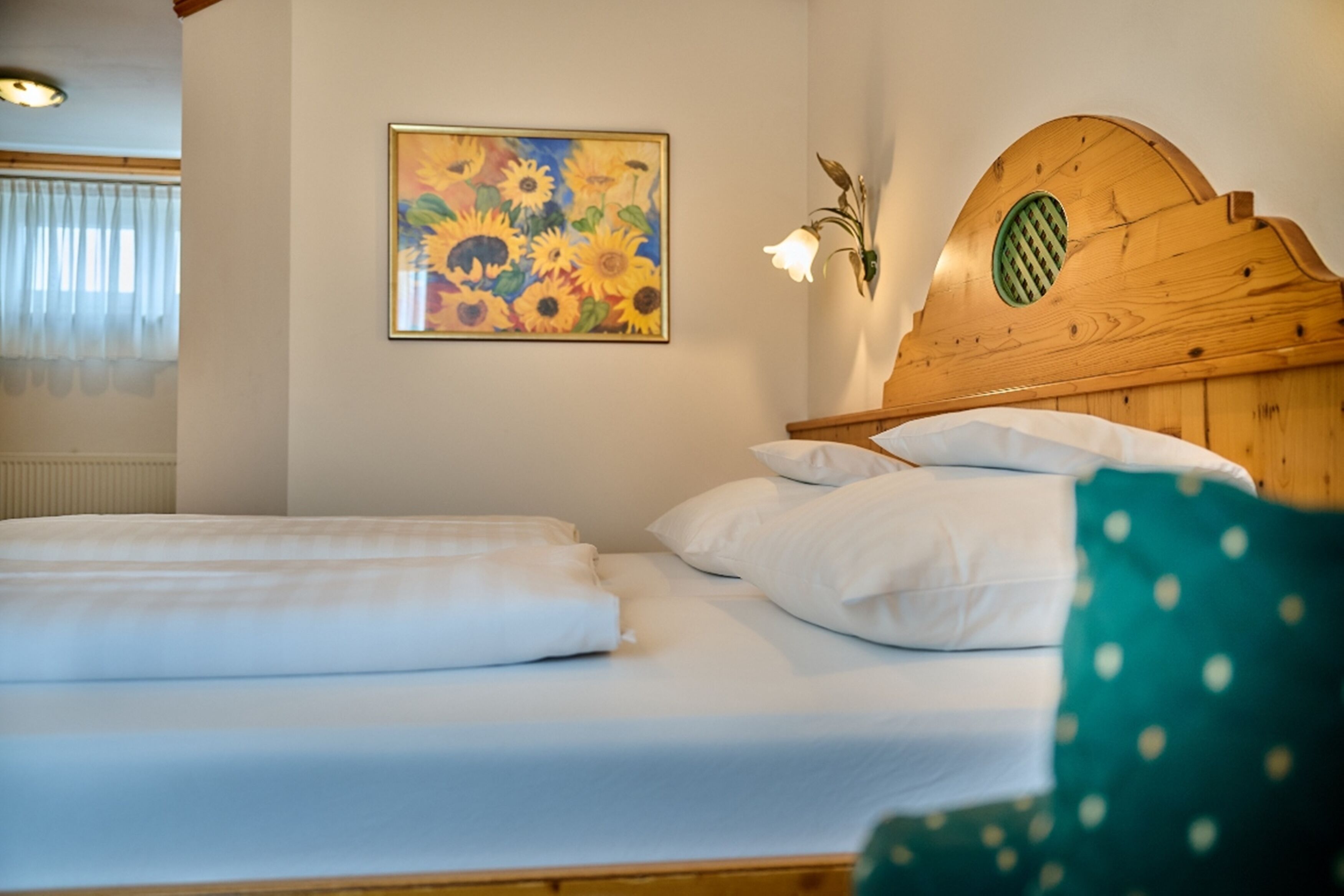 A neatly made bed with white linens, a wooden headboard, and a sunflower painting on the wall.