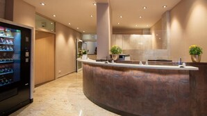 A modern reception area with a curved counter, a vending machine, and potted plants. - Garni Hotel Schumacher (Filderstadt)