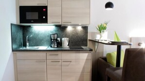 A compact kitchen with a microwave, coffee maker, and sink. There is a small dining area with a chair and a table. - Garni Hotel Schumacher (Filderstadt)