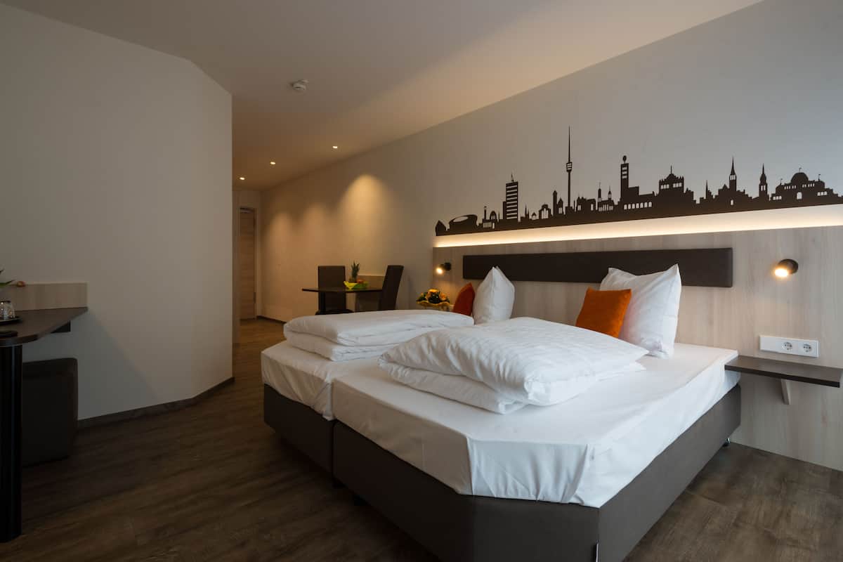 A modern hotel room with a large bed, a desk, and a city skyline wall art.