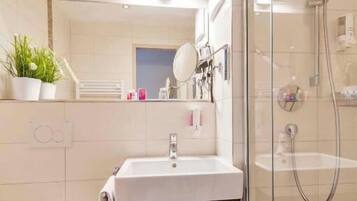 Ein modernes Badezimmer mit einer Duschkabine, einem weißen Waschbecken mit Handtuchhalter und einem kleinen Ablagefach für Pflegeprodukte.