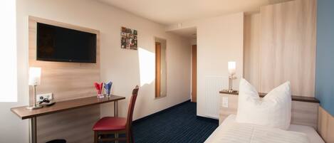 A hotel room with a bed, a desk, a chair, a TV, and a window.