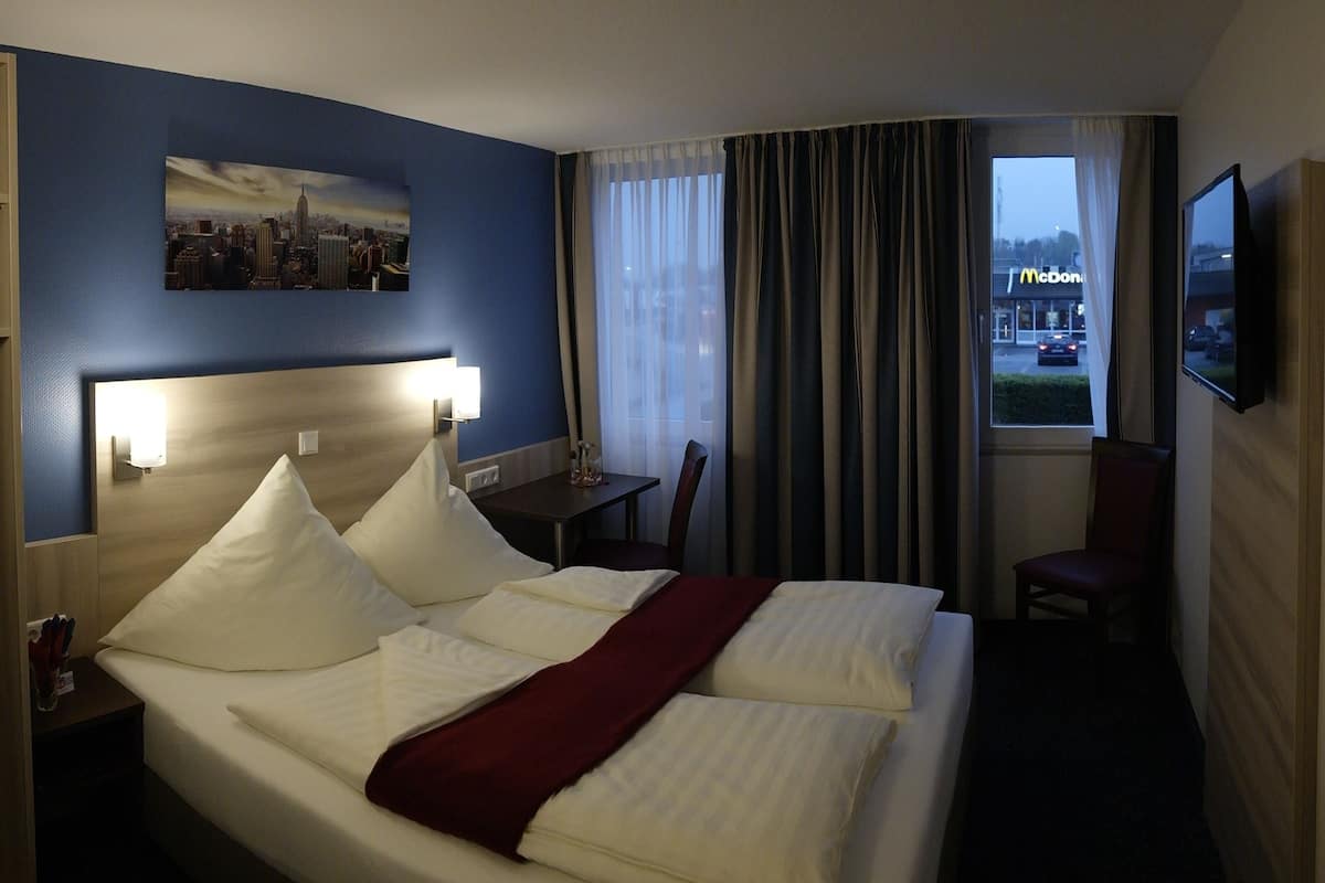 A hotel room with a bed, a desk, a chair, a TV, and a window with curtains.