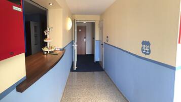A hotel hallway with a reception desk, a check-out counter, and a door with a number sign.