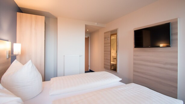A hotel room with two beds, a TV mounted on the wall, and a bathroom visible through an open door. - Motel 44 (Geseke)