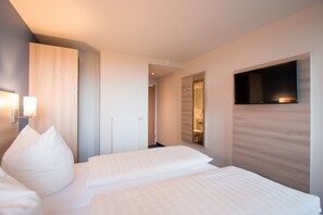 Habitación de hotel con dos camas, un televisor montado en la pared y un baño visible a través de una puerta abierta.
