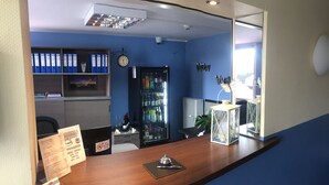 A reception desk with a clock, a no smoking sign, a wine cooler, and a reception counter with a menu board. - Motel 44 (Geseke)