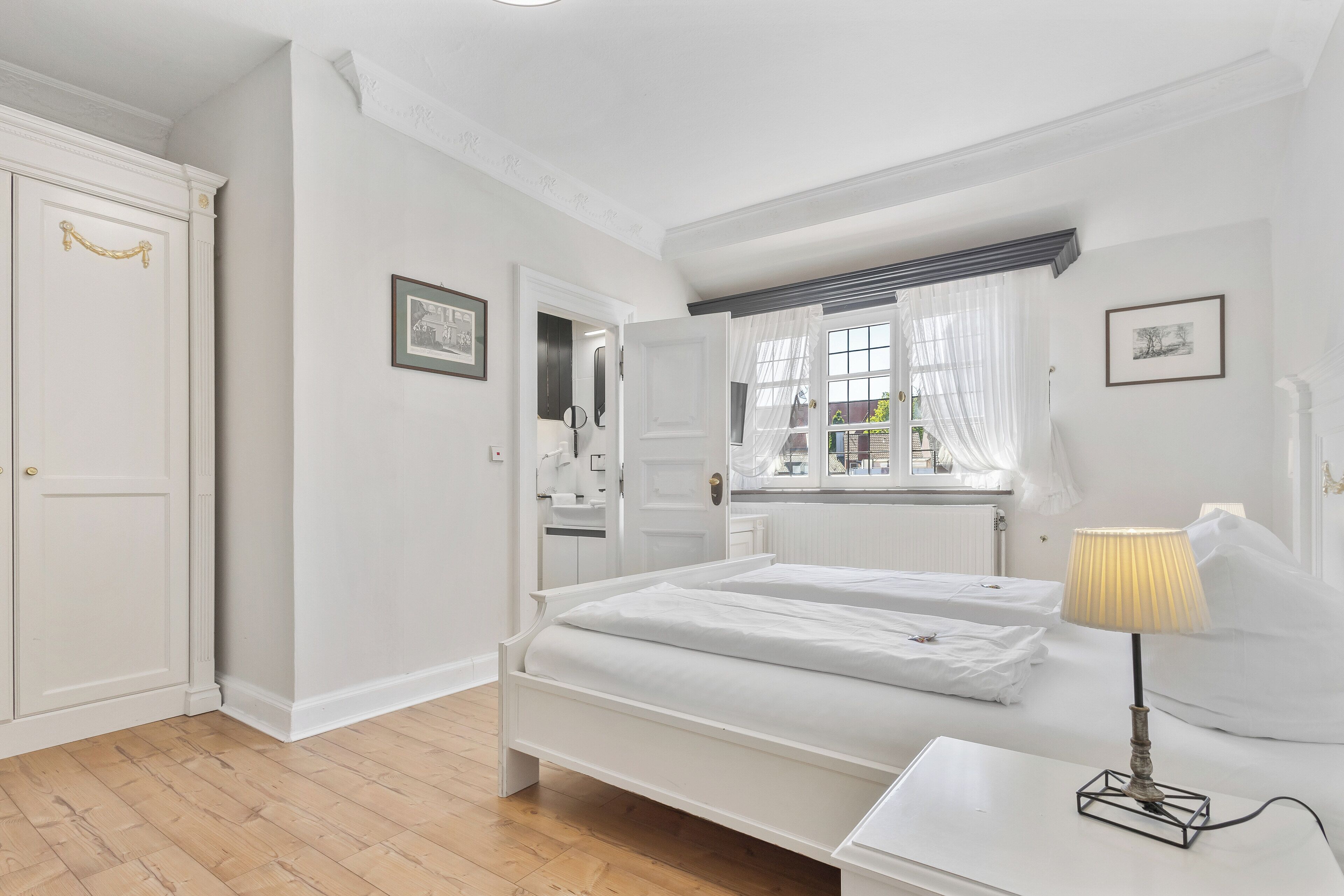 Une chambre à coucher avec un lit double, une table de chevet avec une lampe, une armoire et une fenêtre avec des rideaux.