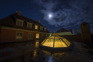 Uma estrutura de vidro hexagonal num pátio sob um céu noturno com uma lua cheia.