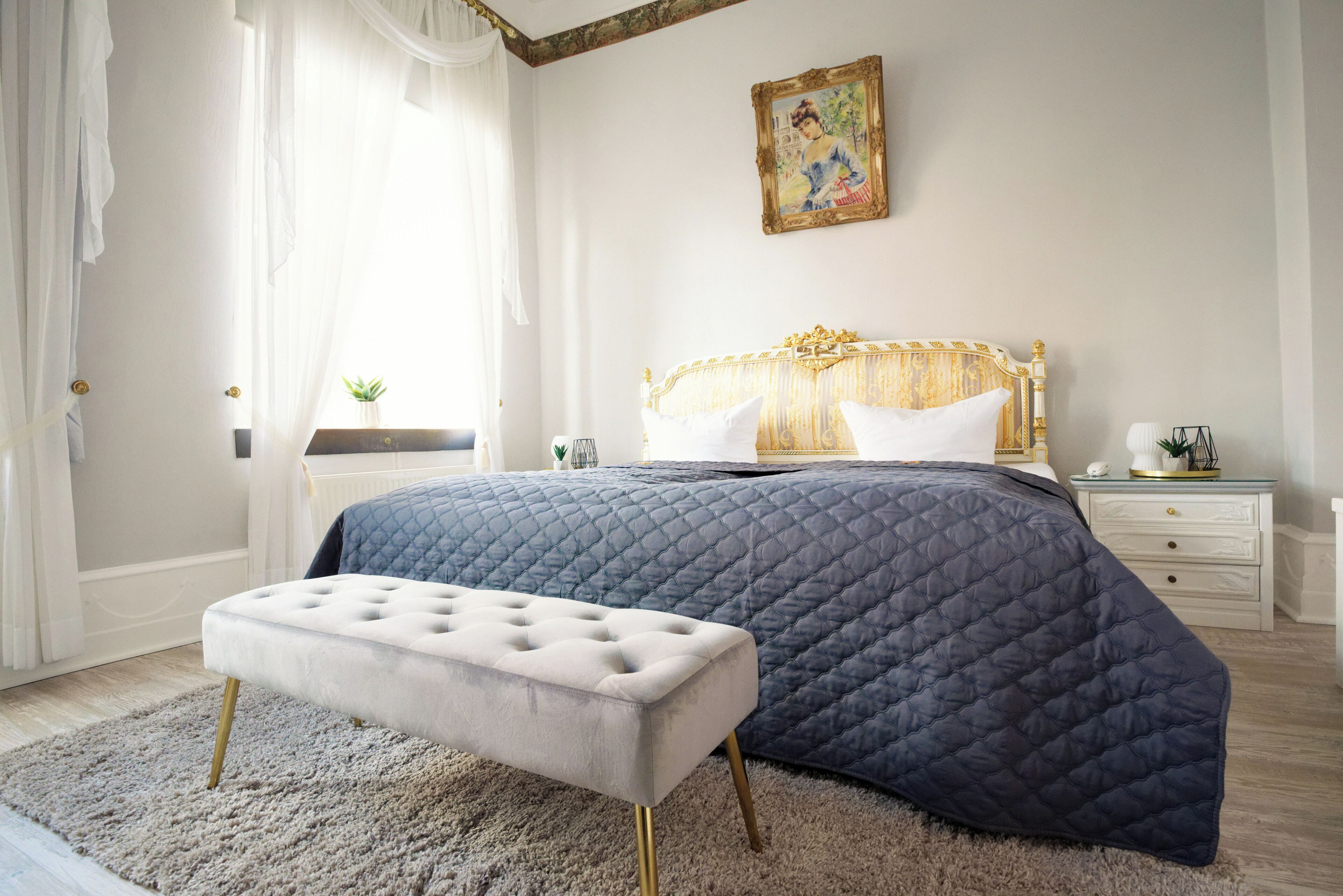 Un dormitorio con una cama grande, una mesita de noche, una ventana con cortinas y un cuadro en la pared.