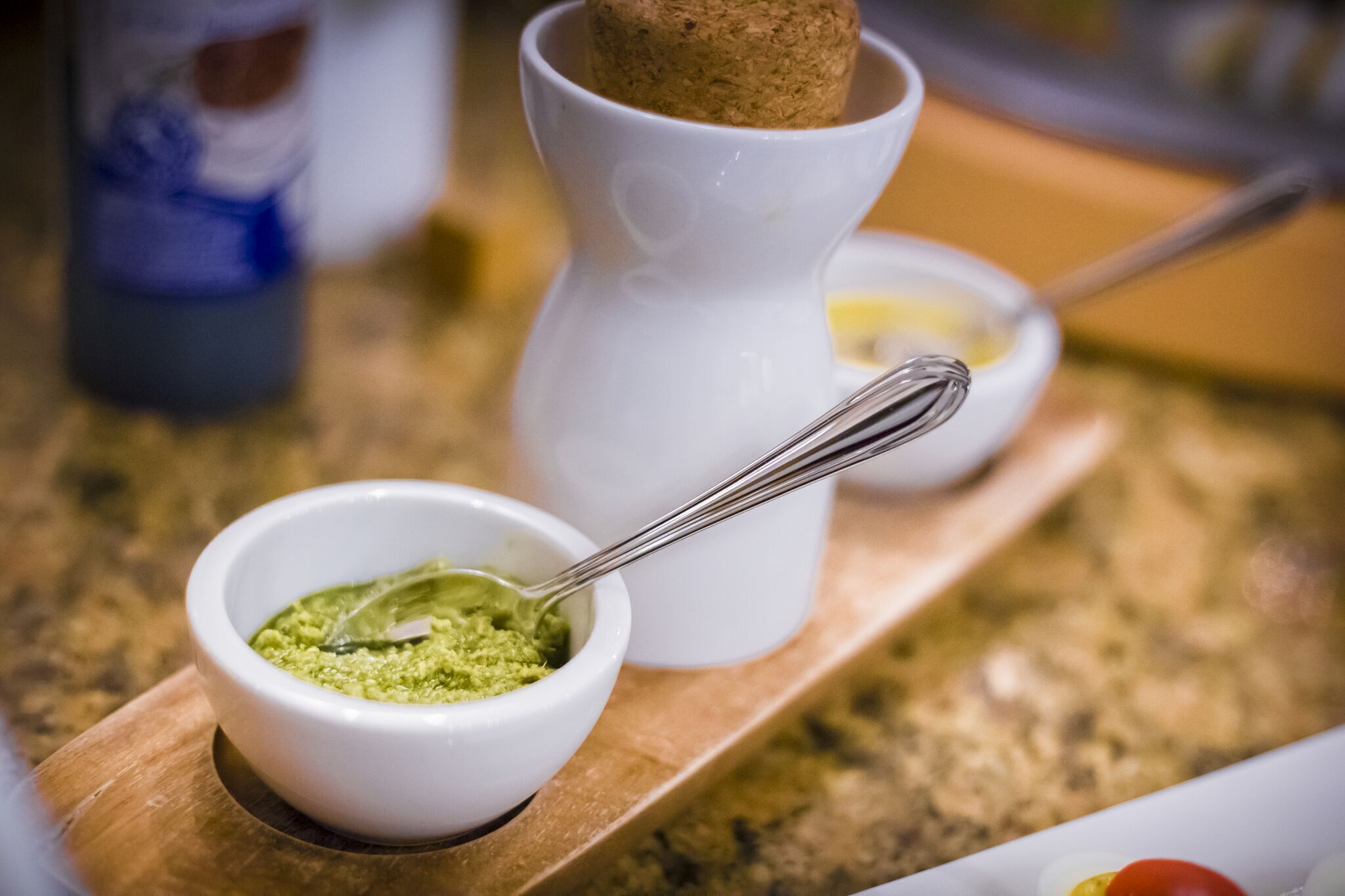 A wooden tray with a white mortar and pestle, a bowl of green substance, and a spoon.