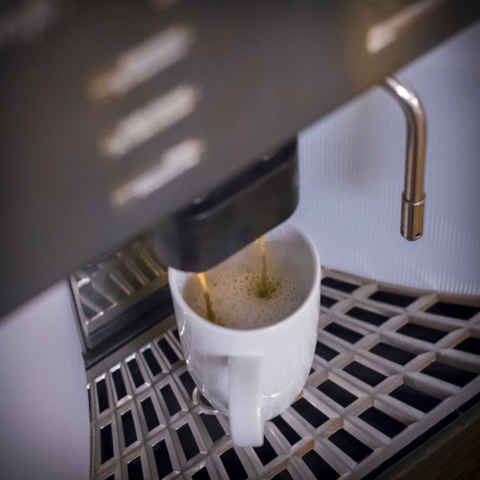 Une machine à café distribue de l’expresso dans une tasse blanche posée sur une grille métallique.