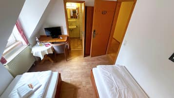 Una habitación pequeña y triangular con dos camas, un escritorio y baño.