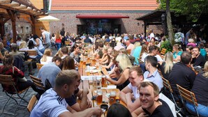 An outdoor dining area with wooden tables and benches, surrounded by brick buildings with a red-tiled roof. - Brauhaus Wiesenmühle (Fulda)