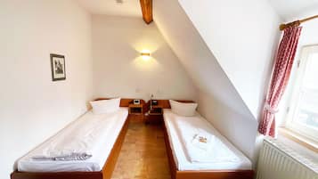 A small, triangular room with two single beds, a wooden ceiling beam, a wall-mounted light, and a radiator.