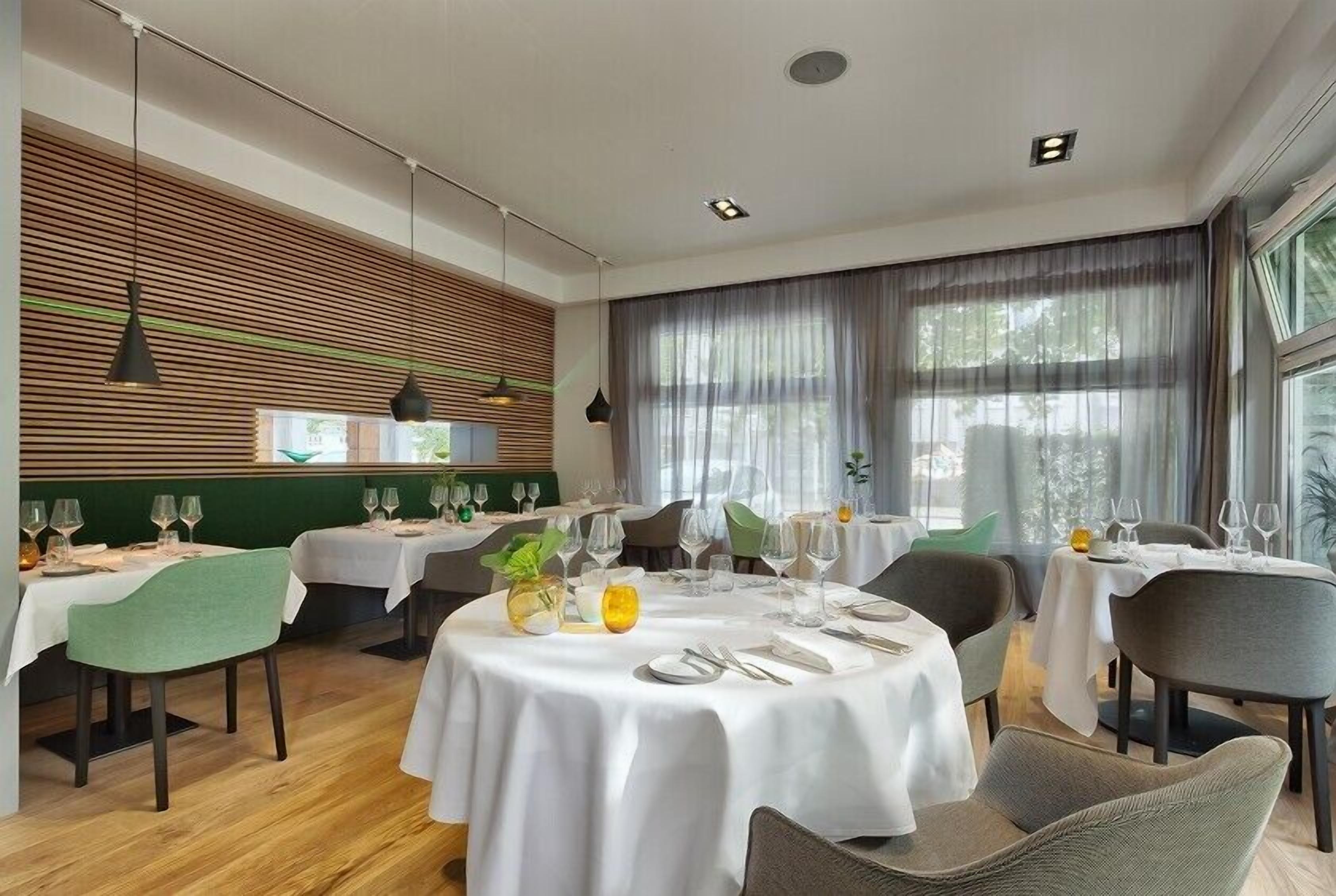 A restaurant with round tables, green chairs, and a wooden slat wall.