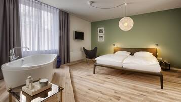 Quarto moderno com uma banheira grande, cama com roupa de cama branca, piso de madeira e uma parede verde.