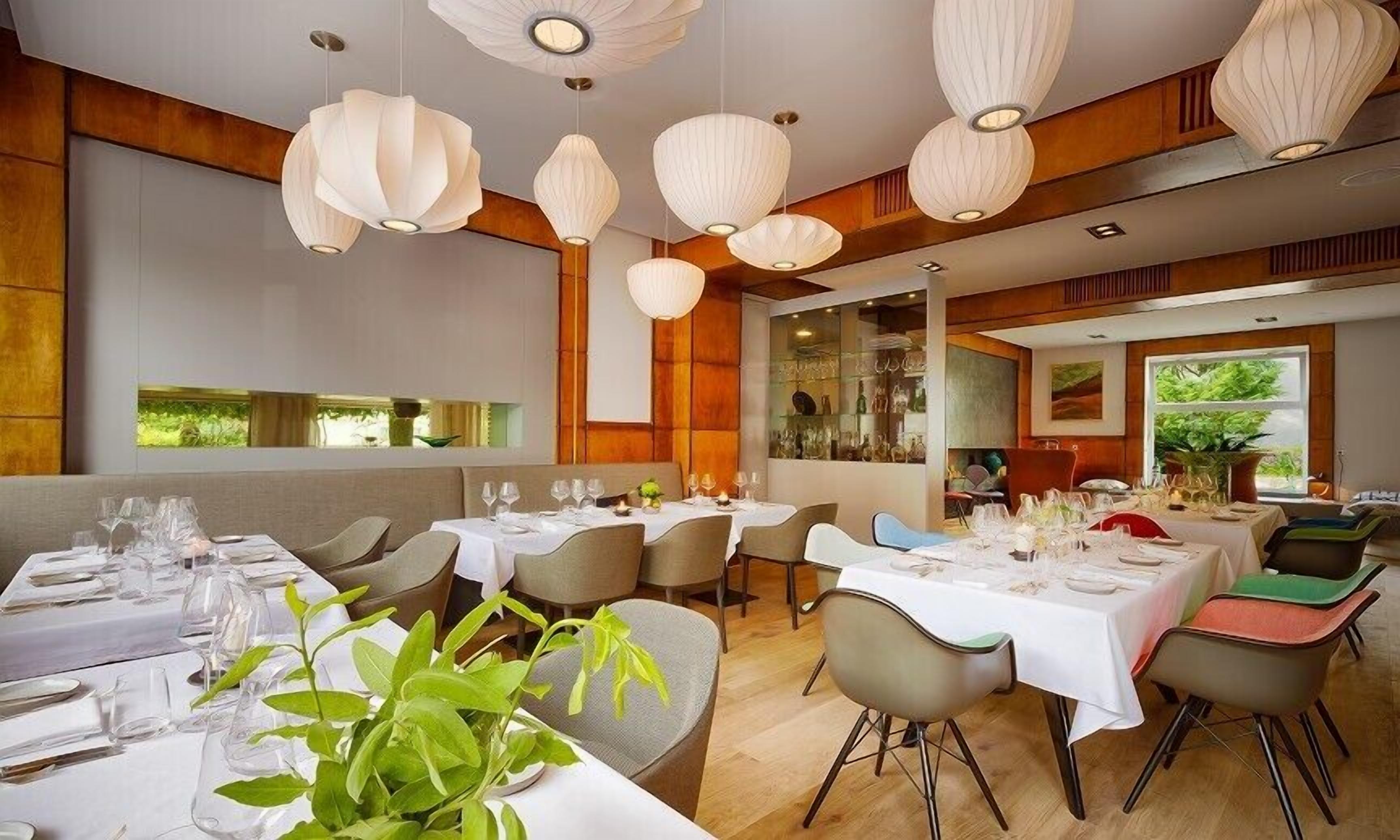 A restaurant with multiple tables set for dining, featuring a modern interior with wooden accents and hanging pendant lights.