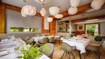 A restaurant with multiple tables set for dining, featuring a modern interior with wooden accents and hanging pendant lights.