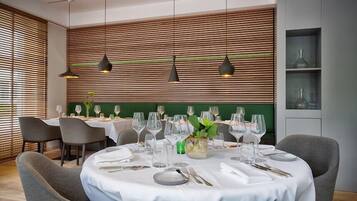 Un comedor con mesas redondas dispuestas para una comida, con una pared verde con listones de madera horizontales e iluminación colgante.