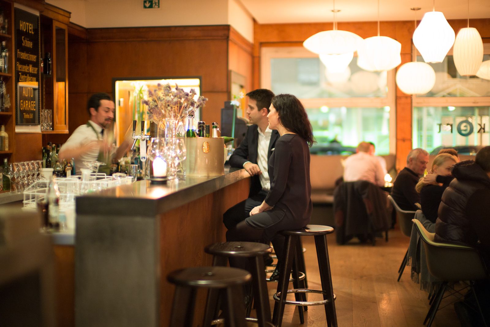 Un espace bar avec des tabourets, un comptoir et un barman. On aperçoit des tables et des chaises au fond.